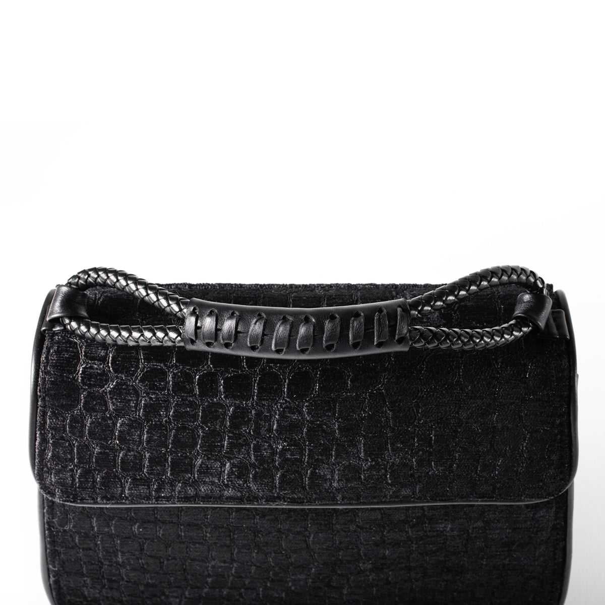 A close-up of a black textured handbag with a crocodile-embossed pattern and a braided top handle, shown against a plain white background.