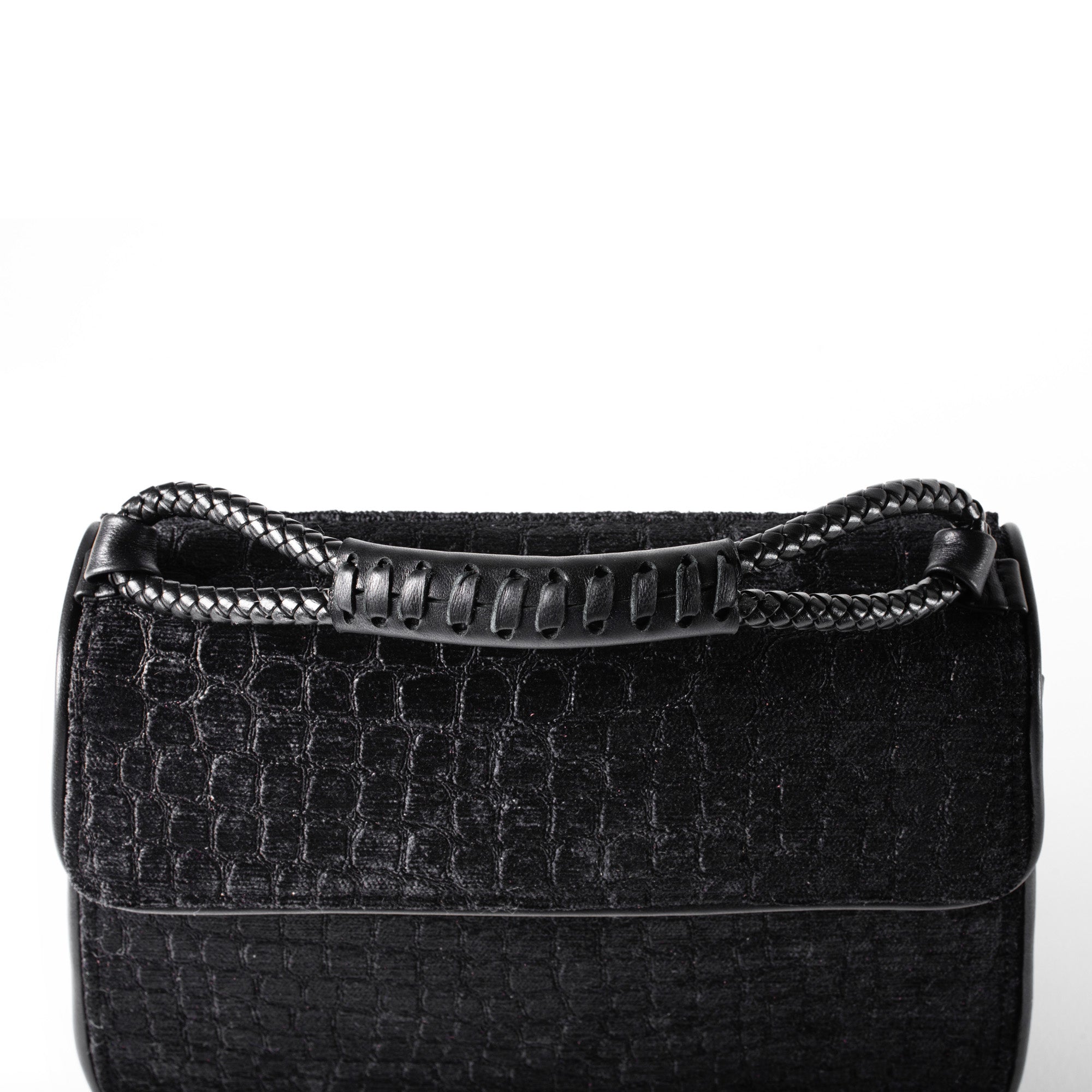 A close-up of a black textured handbag with a crocodile-embossed pattern and a braided top handle, shown against a plain white background.