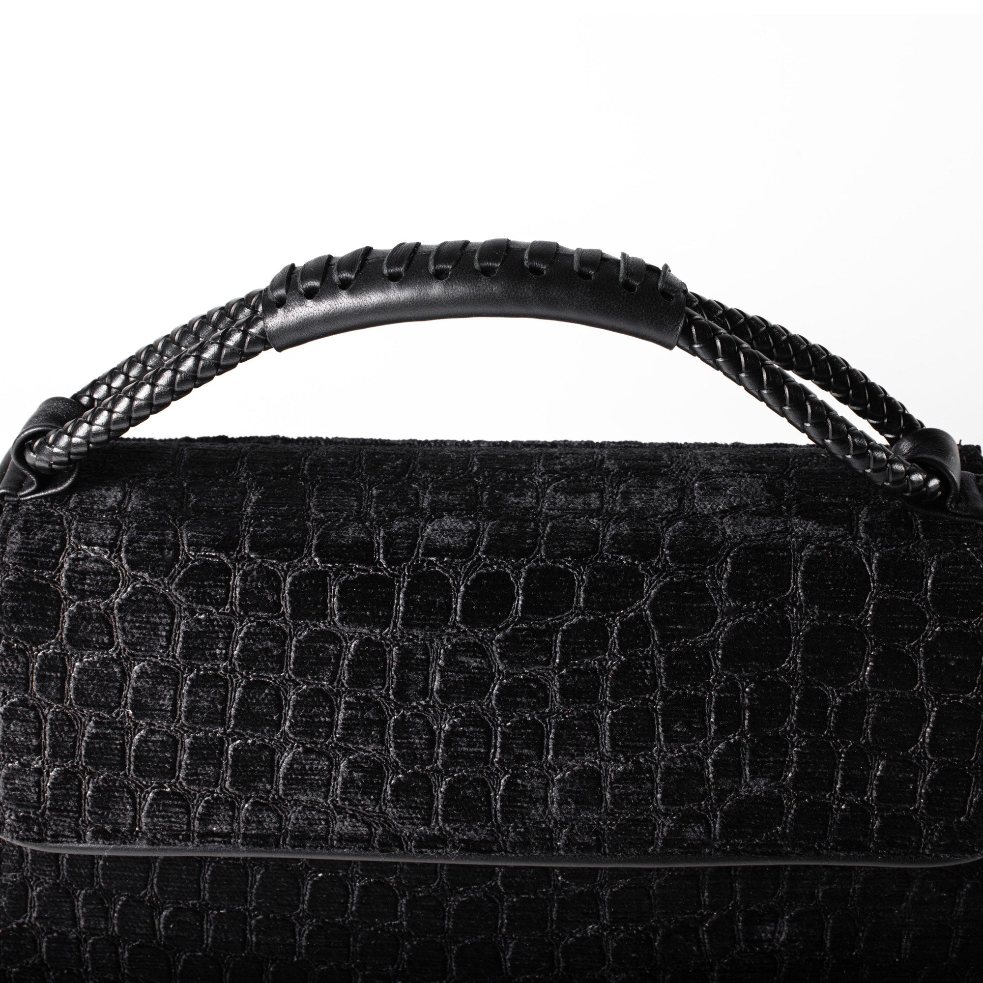 Close-up of a black textured handbag with a crocodile-embossed pattern and a braided top handle against a white background.