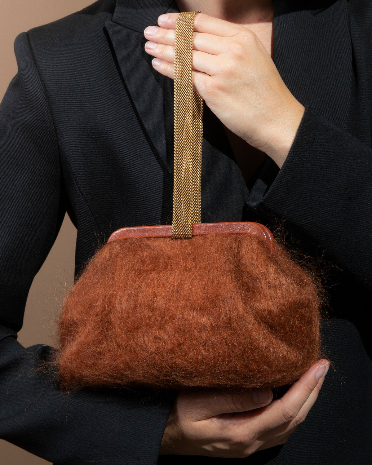 Person holding a brown textured handbag against a beige background