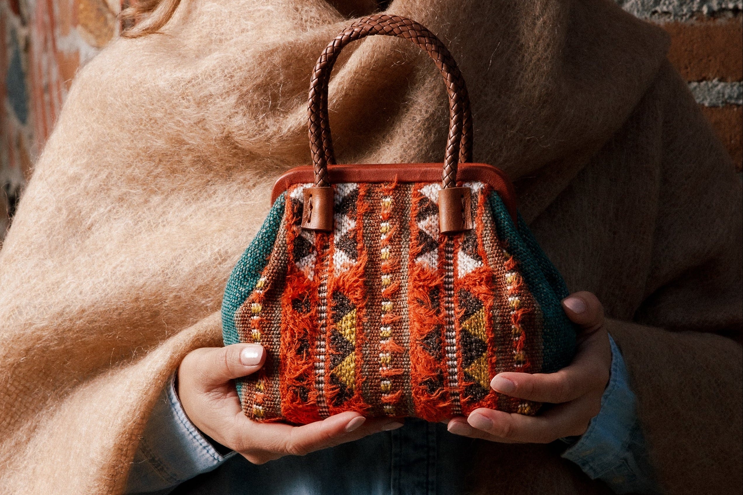 Woman holding a patterned handbag against a brick wall.