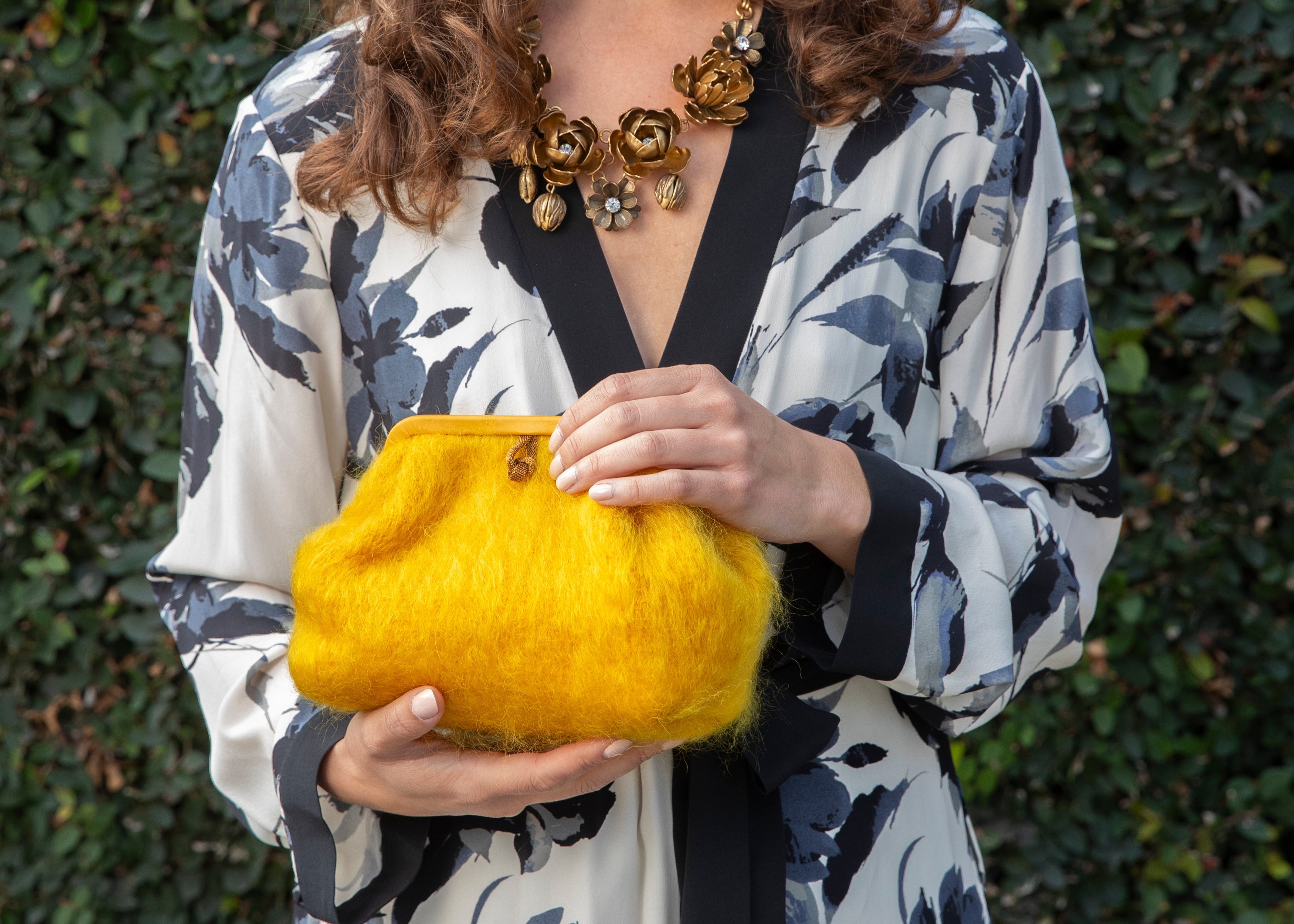 Woman holding a yellow clutch against a green leafy background
