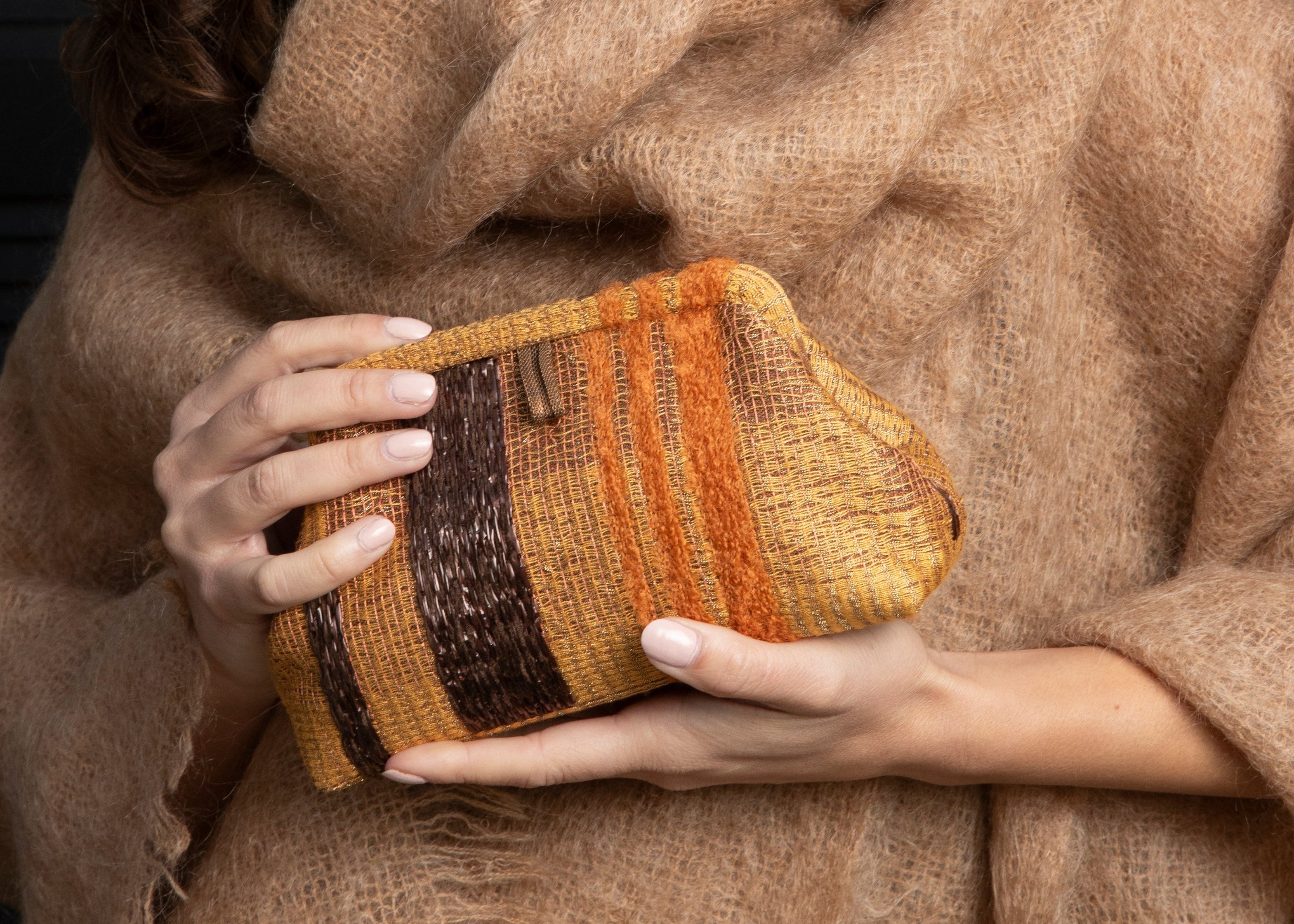 Woman wrapped in a brown blanket holding a colorful clutch against a blurred indoor background